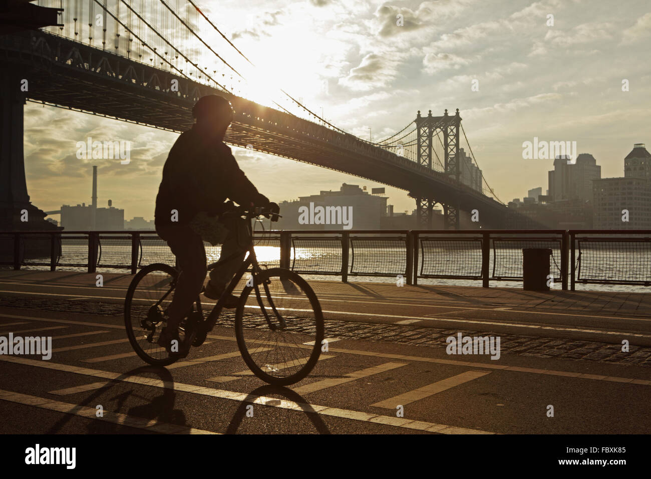 Sunrise over the Manhattan Bridge New York City morning as a cyclist pedals south  down the East River Esplanade Stock Photo