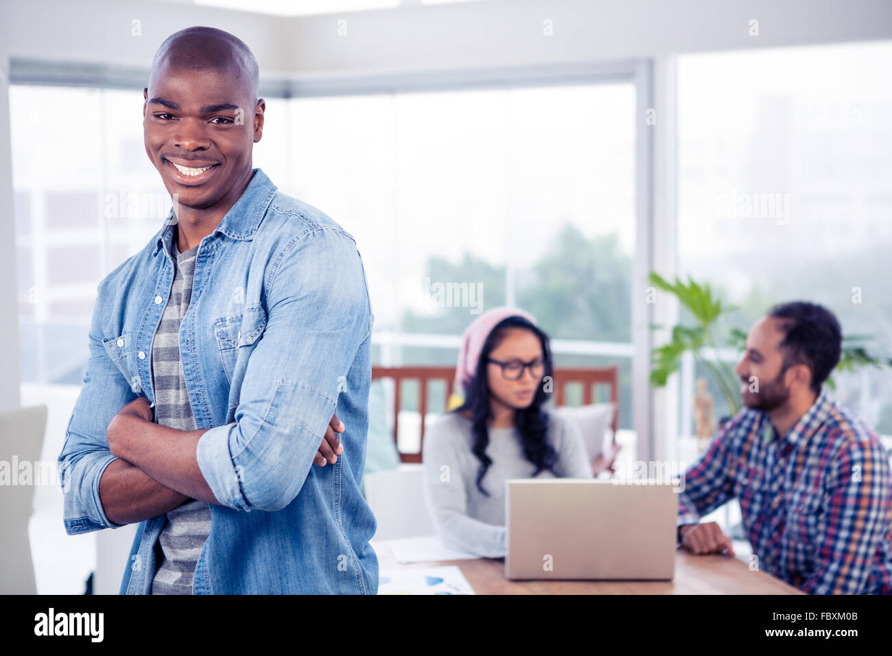 Portrait of smiling businessman standing with arms crossed in office ...