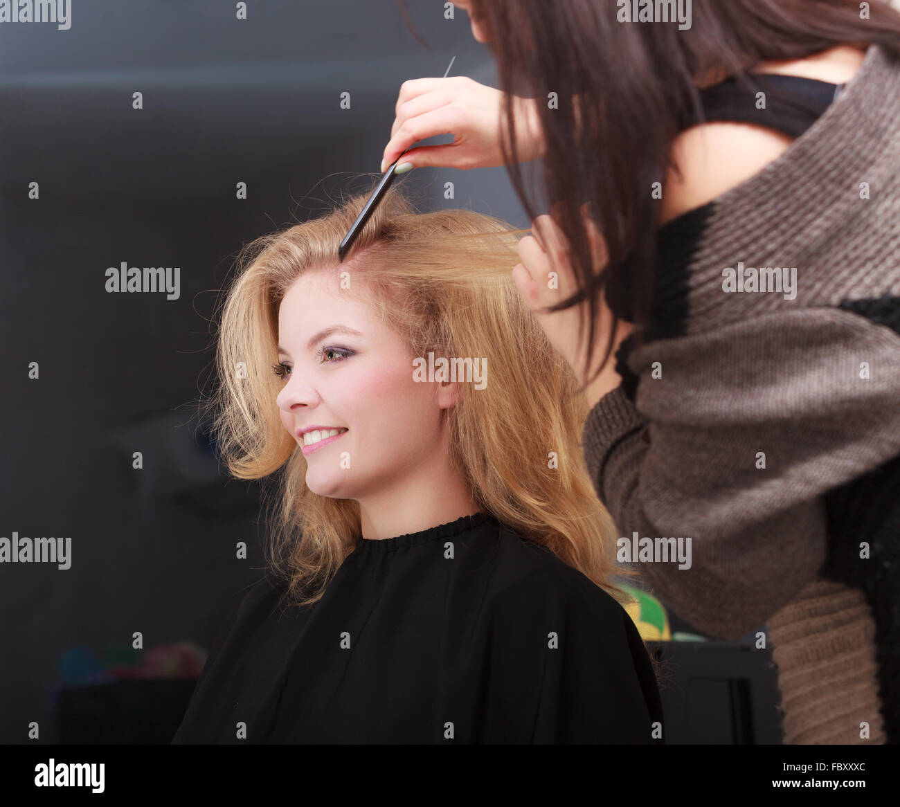 Beautiful smiling girl with blond wavy hair by hairdresser. Hairstylist combing female client. Young woman in hairdressing beaut Stock Photo