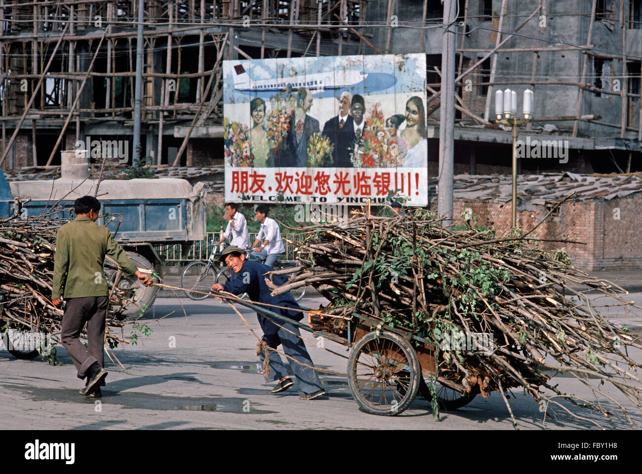 Human power pulling cart load of tree branches in front of welcome to Yinchuan poster, Yinchuan, Ningxia Autonomous Region, China Stock Photo