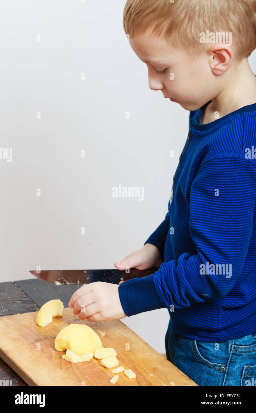Blond boy child kid preschooler with kitchen knife cutting fruit apple Stock Photo