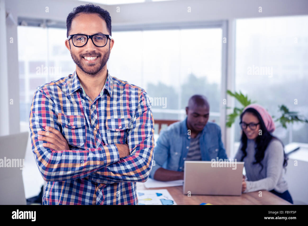 Portrait of happy businessman standing with arms crossed in office ...