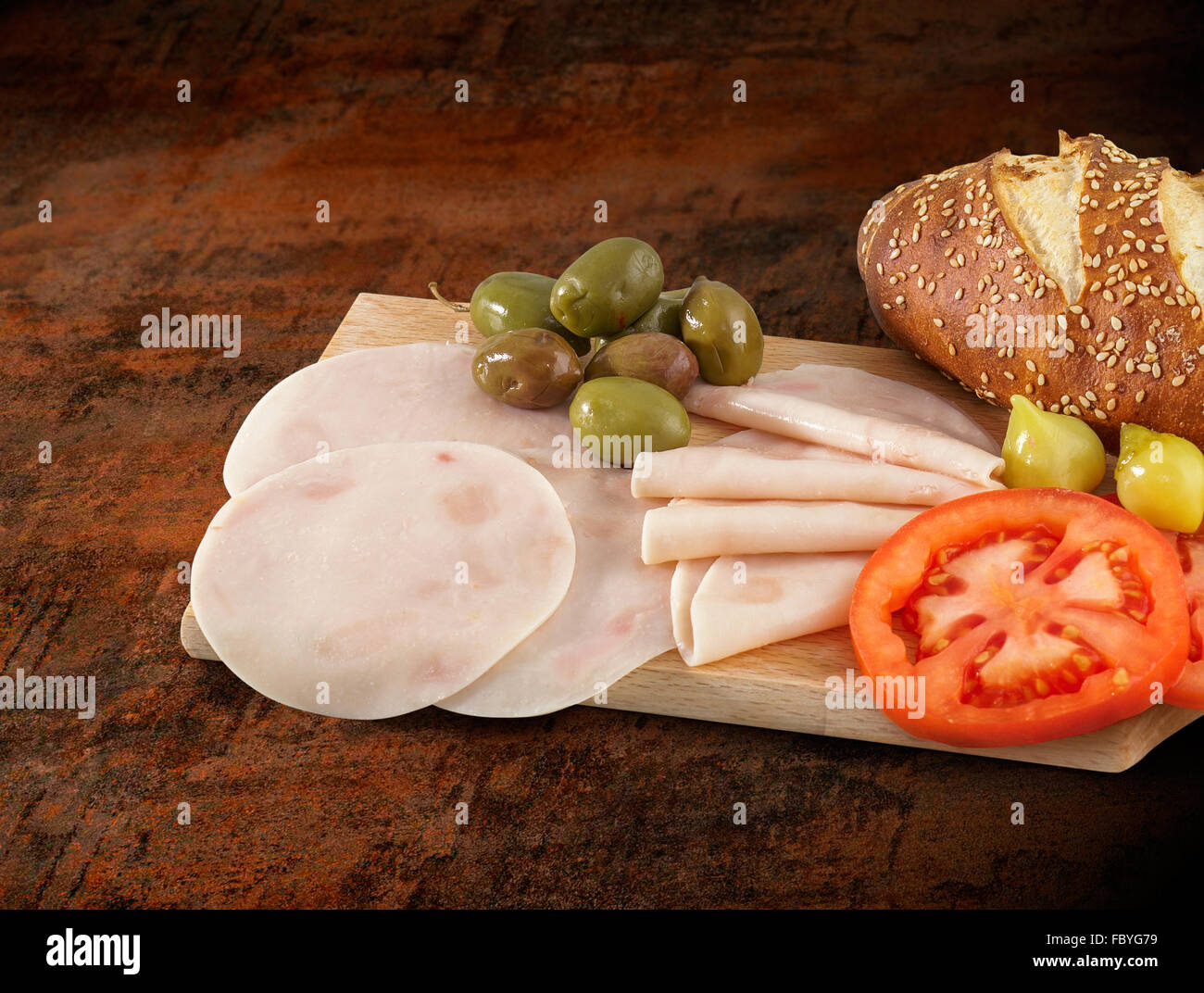Sliced ham salami decorated on wooden board with olives, tomato and lettuce Stock Photo