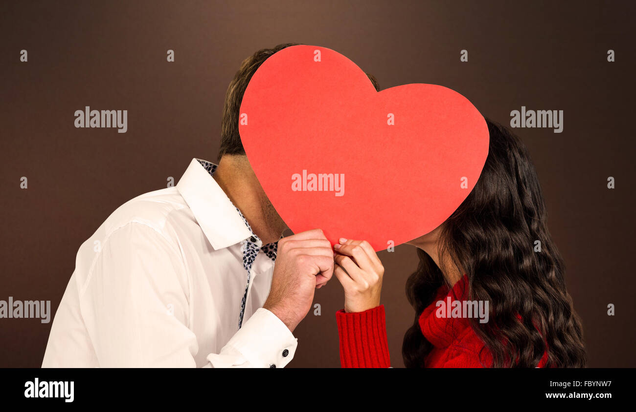 Composite image of couple covering faces with paper heart Stock Photo