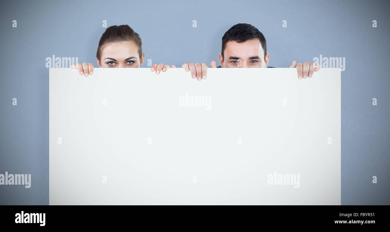 Composite image of business partners hiding behind a sign Stock Photo