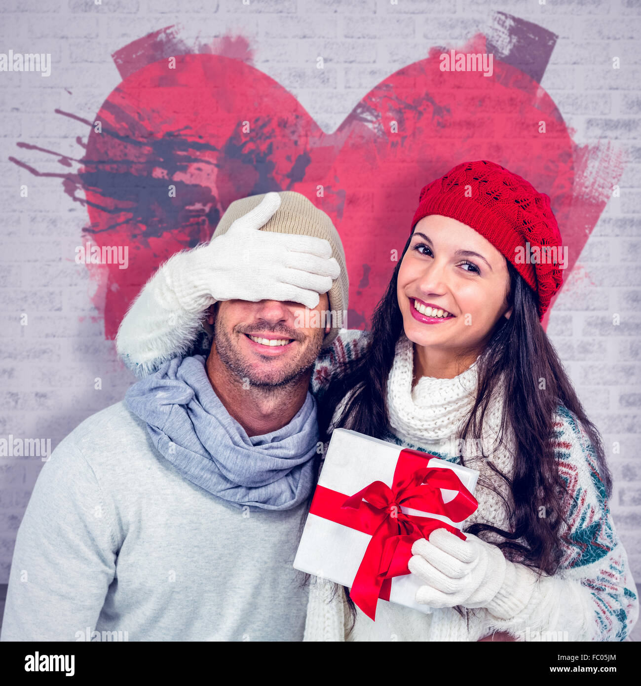 Composite image of smiling woman covering partners eyes and holding gift Stock Photo