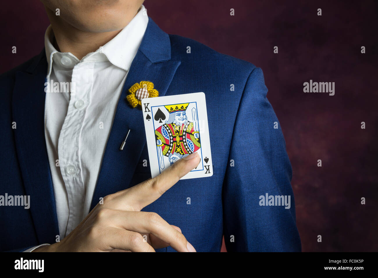 man wearing blue suit, jacket and flower brooch, holding king spades with index and middle finger, casino concept Stock Photo