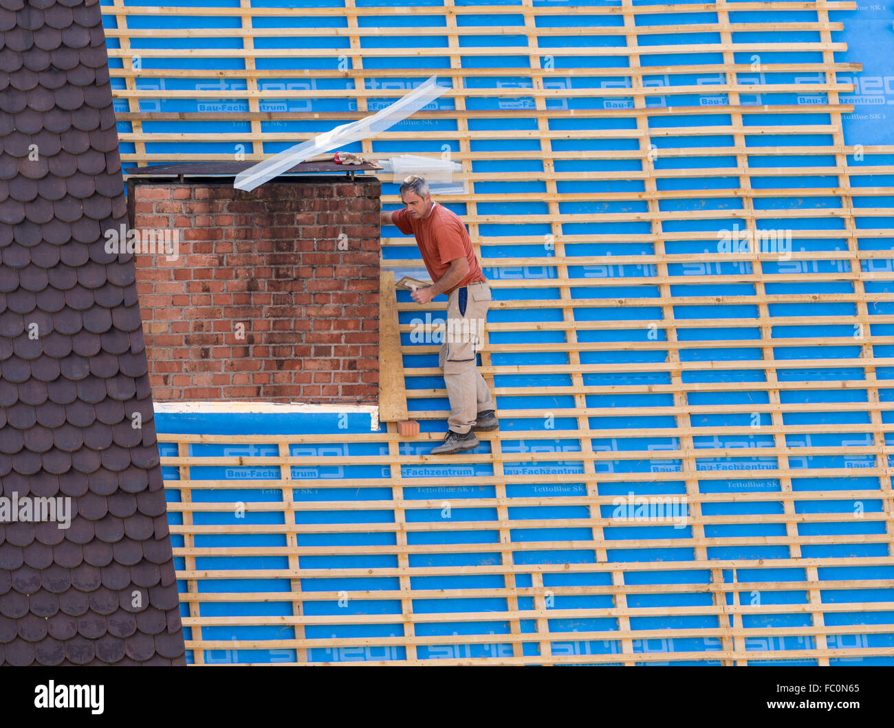Bricklayer on very steep roof in danger of falling Stock Photo
