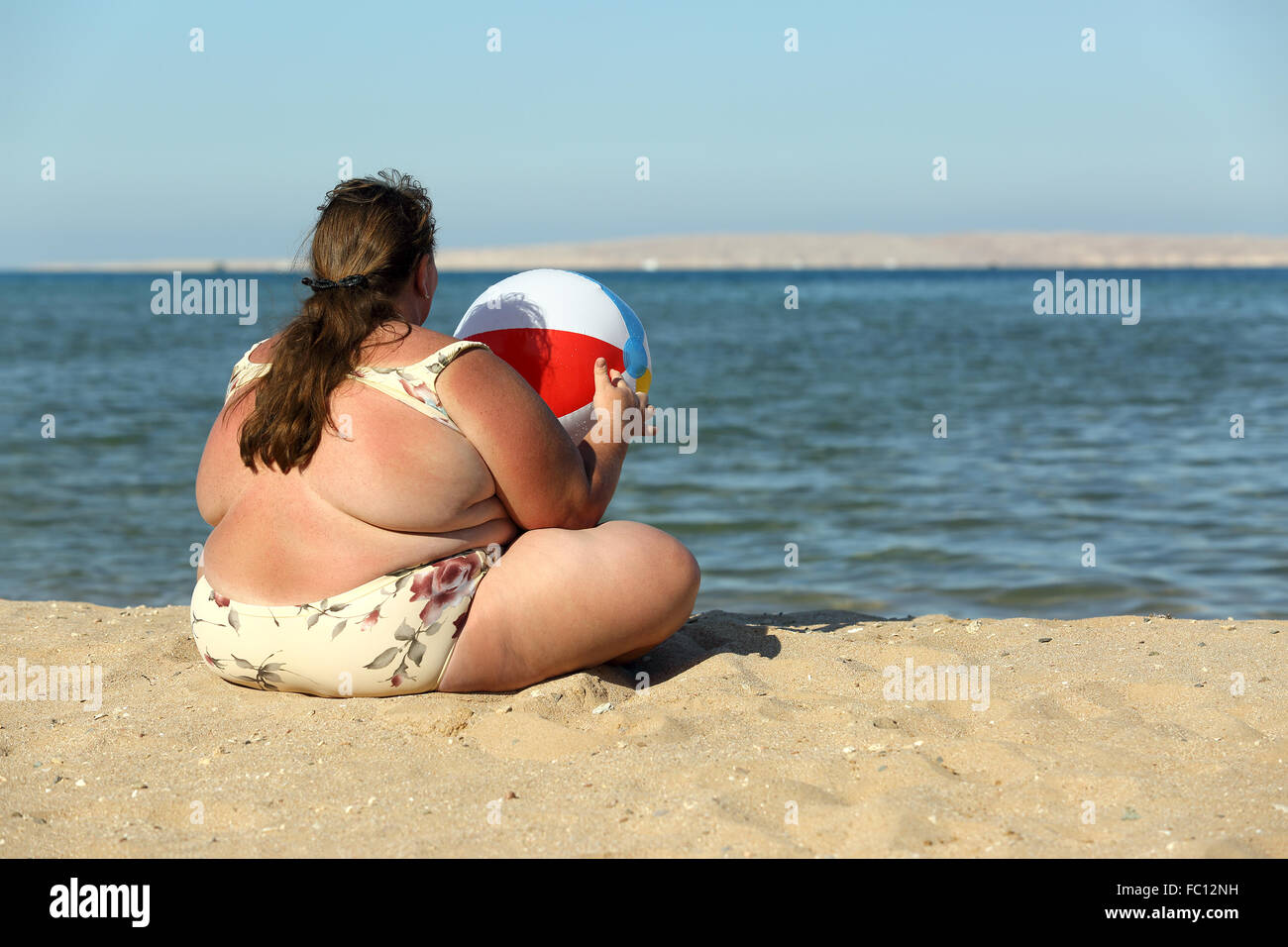 overweight woman with ball on beach Stock Photo