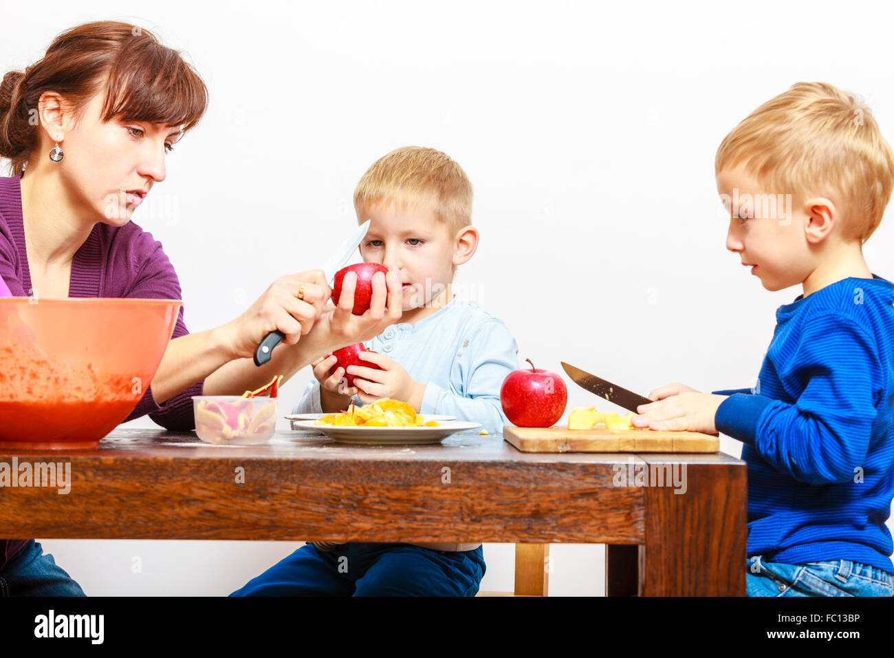 Mother with sons cutting fruits apples at home. Stock Photo