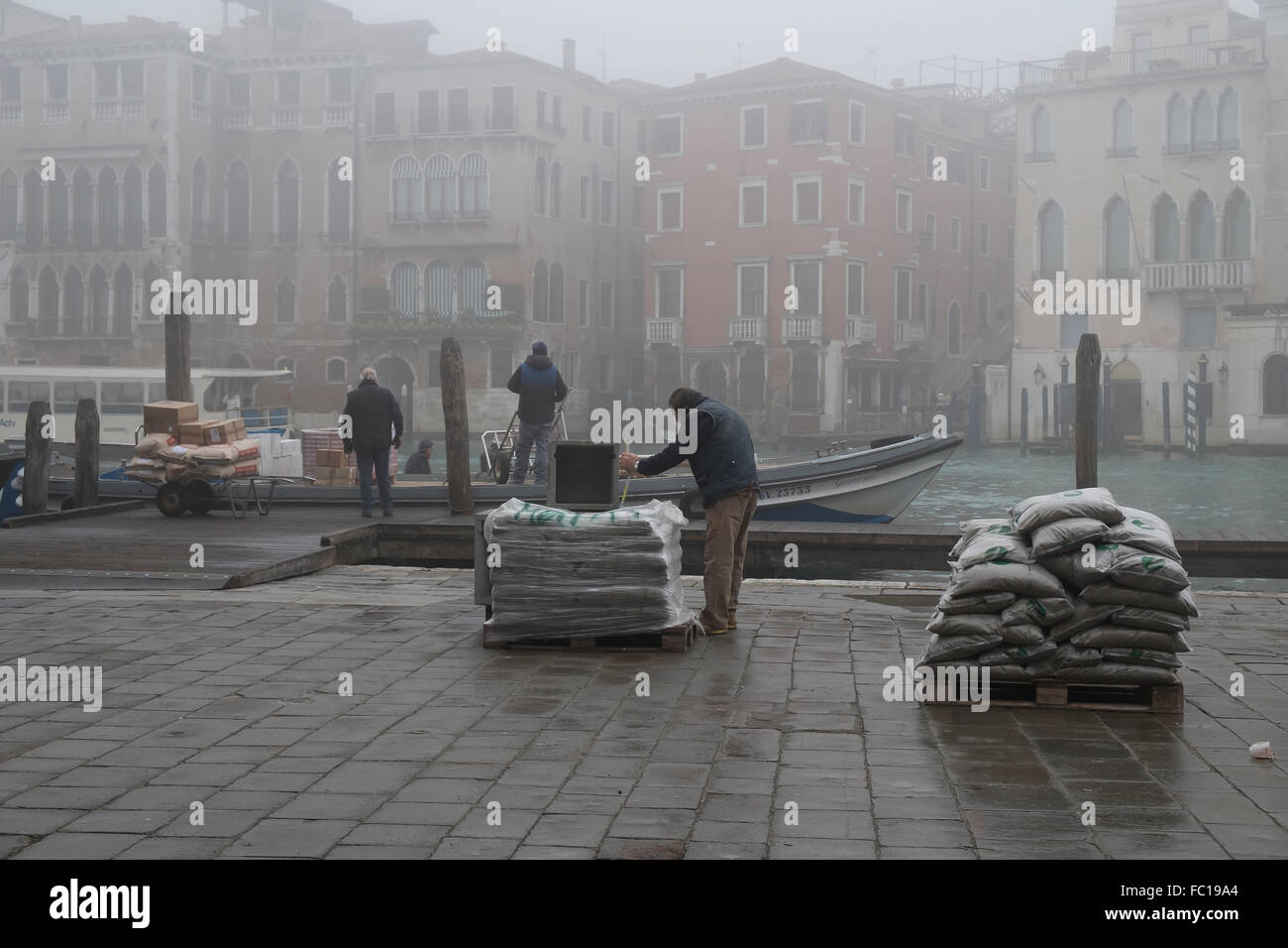 workers unload goods from a boat moored on the Grand Canal in Venice Stock Photo