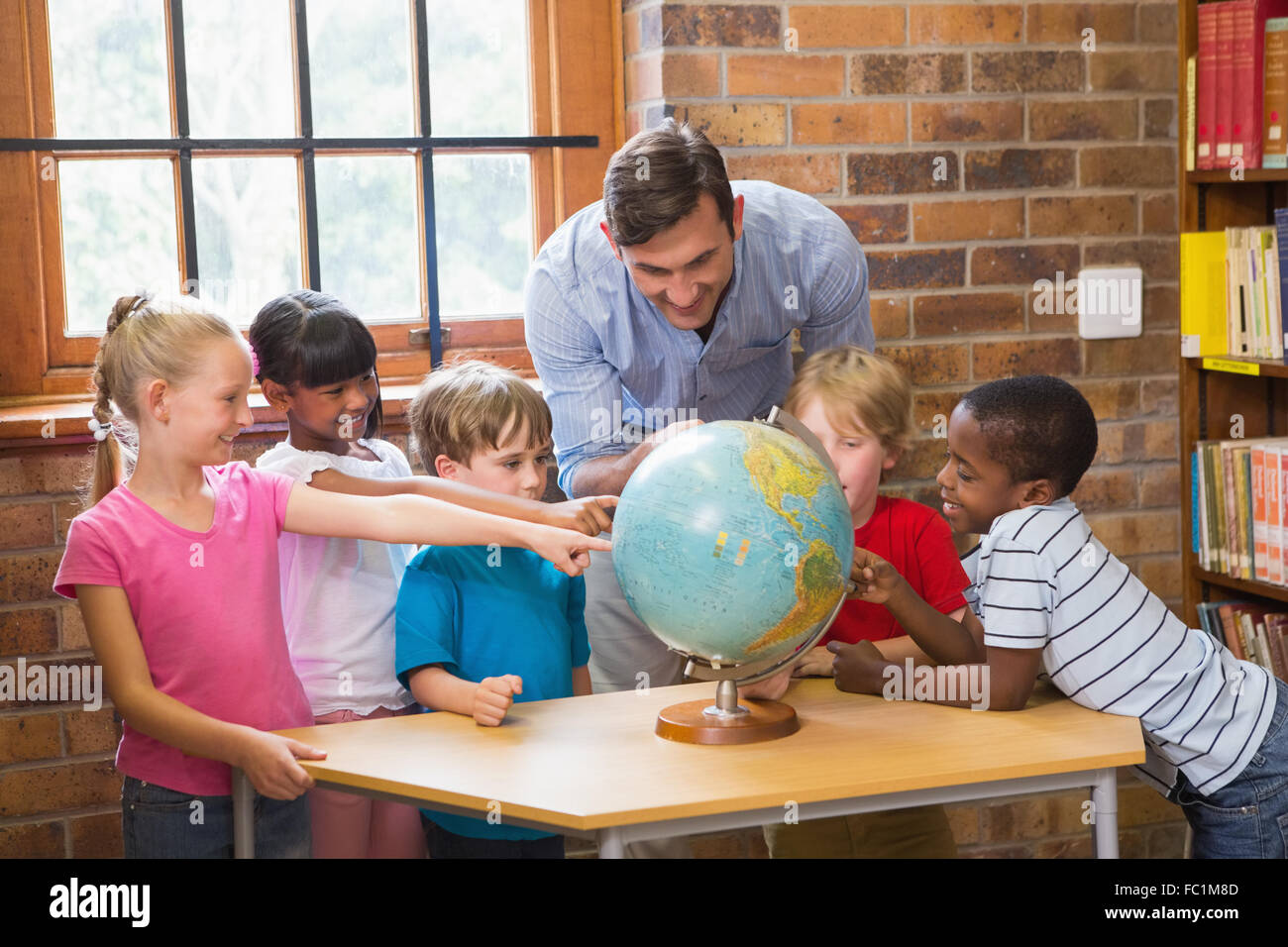 Cute pupils and teacher looking at globe in library Stock Photo - Alamy