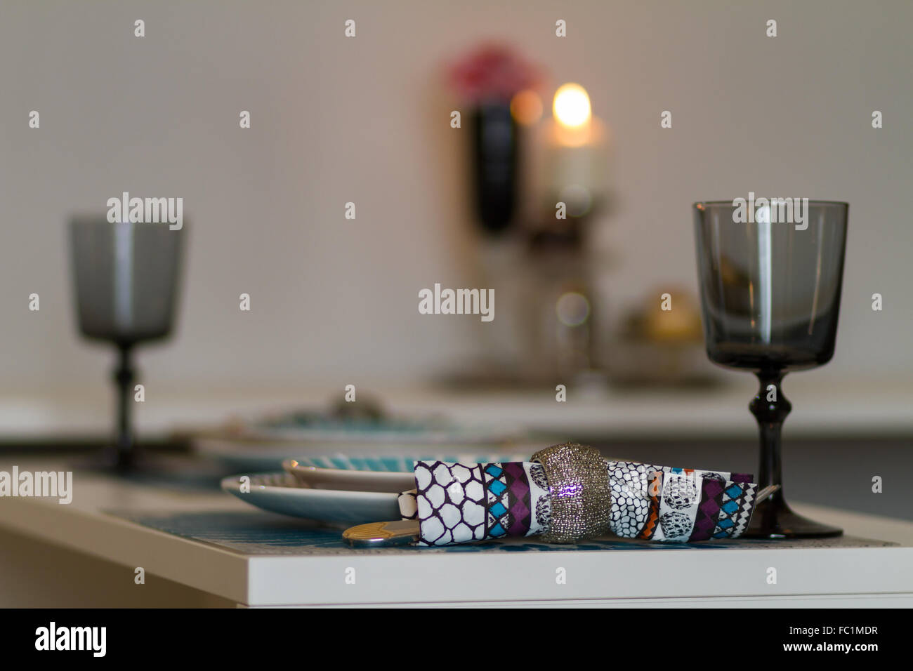 Romantic table set for two people with plates, glasses and cutlery with flower and candle in the background Stock Photo