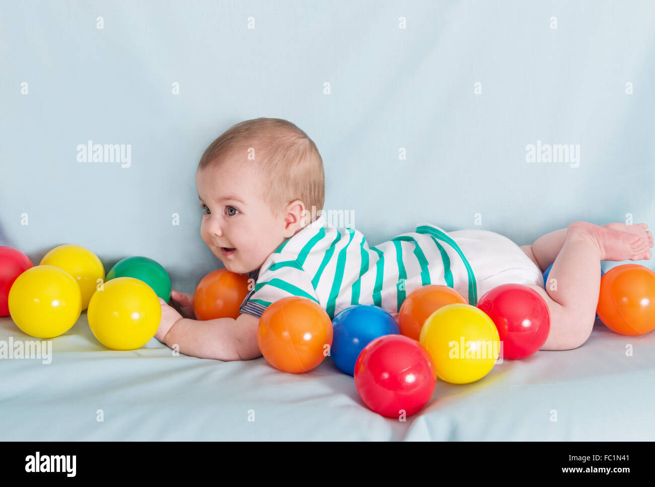 Adorable happy baby boy with multicolored balls on blue background Stock Photo