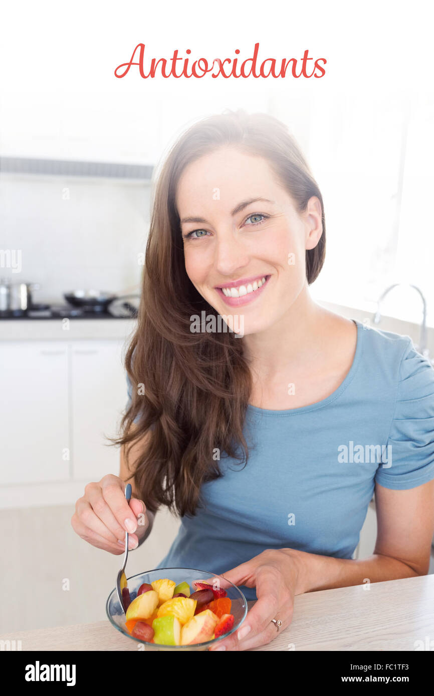 Antioxidants against smiling young woman with fruit salad in kitchen