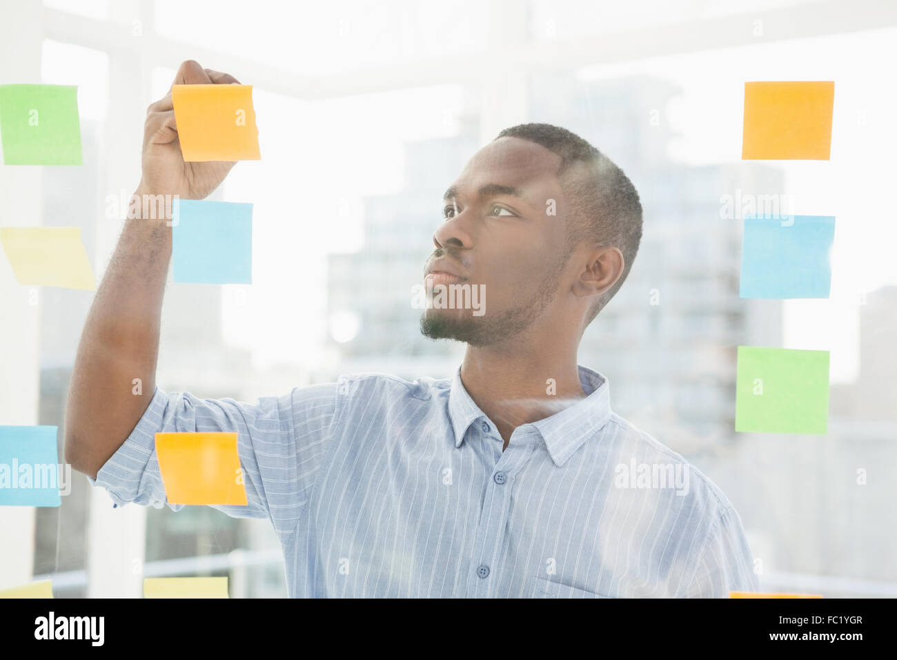 Thoughtful businessman writing on sticky notes on window Stock Photo ...