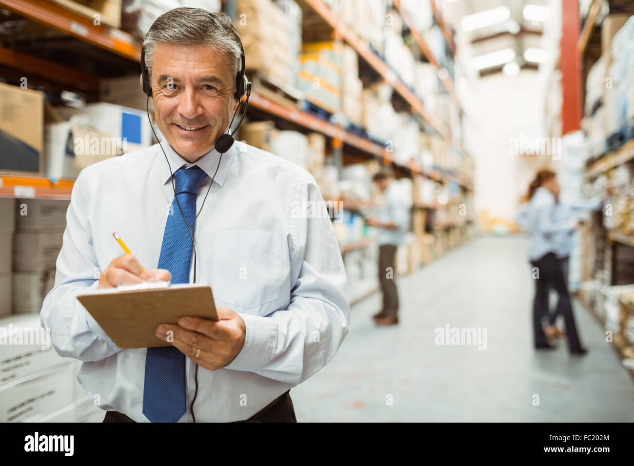 Smiling warehouse manager writing on clipboard Stock Photo