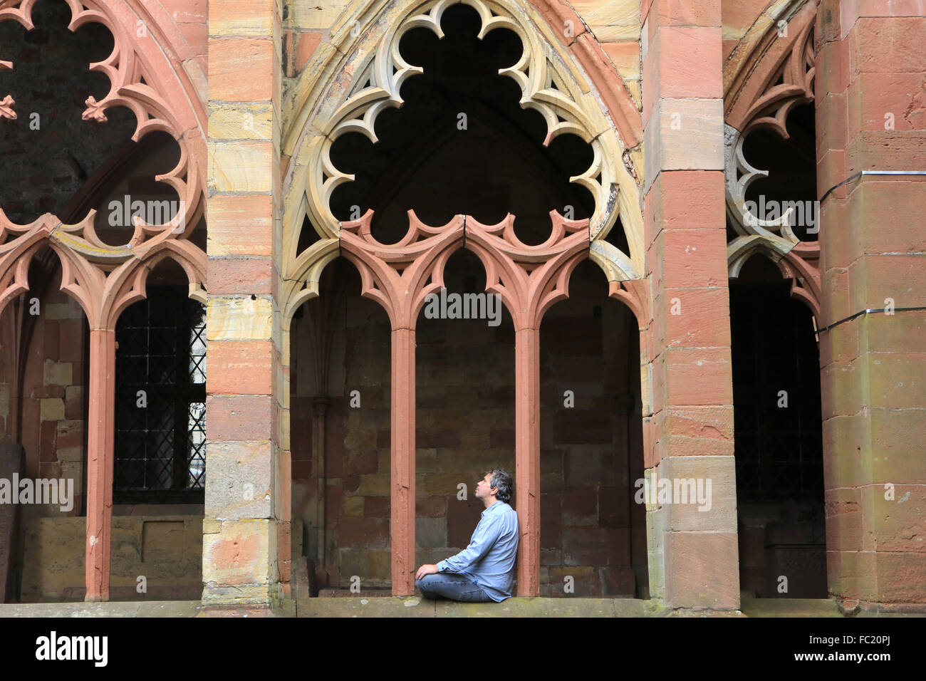 Pilgrim praying in a gothic cloister. Aligning windows of the Gothic cloister. Monolithic columns drums and cubic capitals. Stock Photo