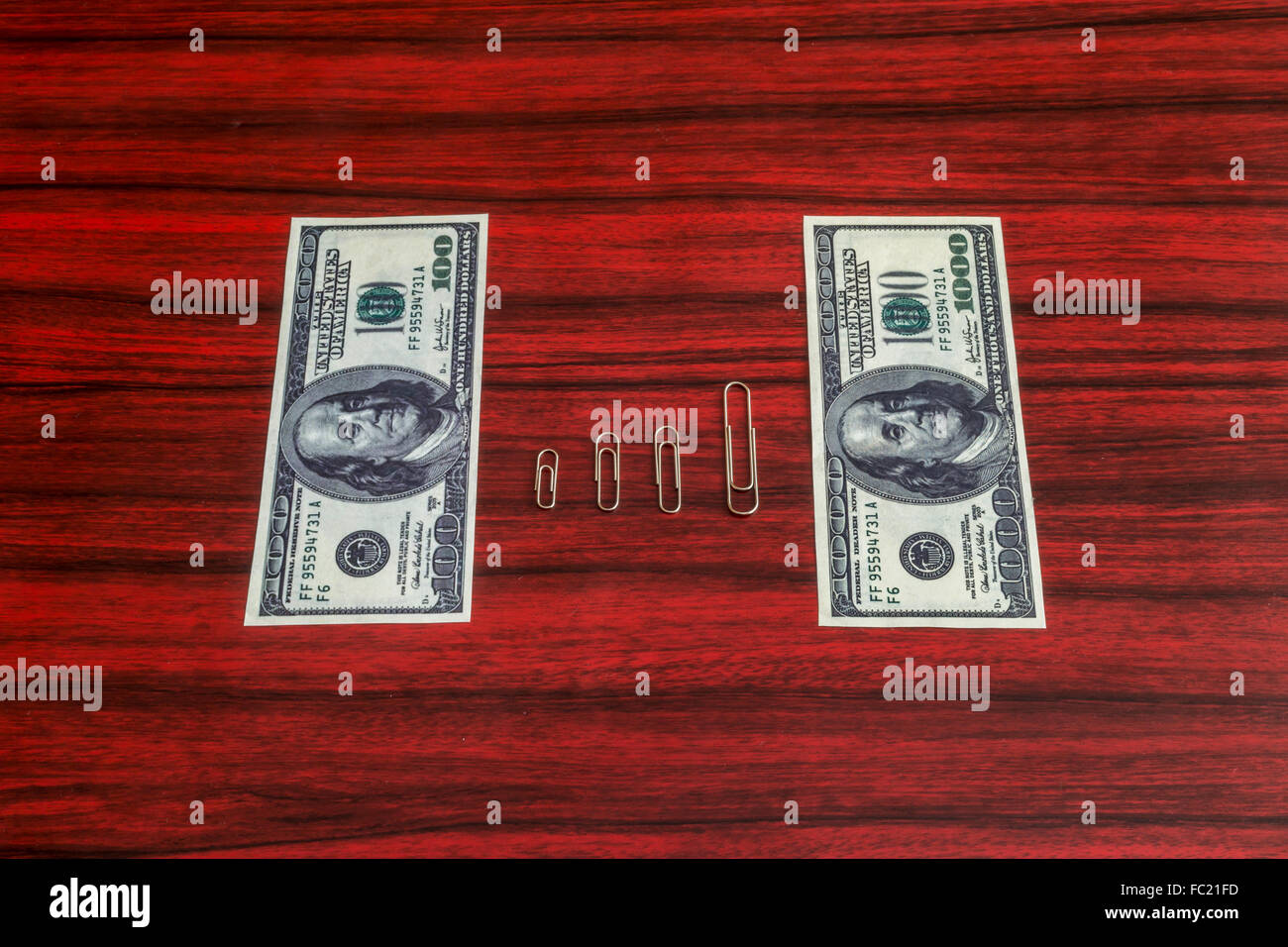 Paper clips arranged by size between 100 and 1000 dollar bill Stock Photo