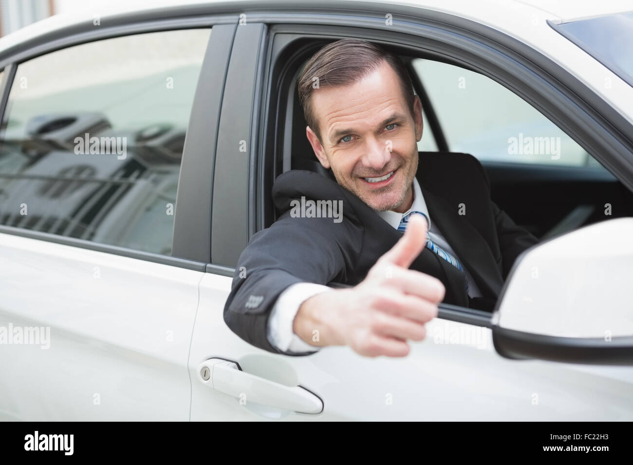 Businessman smiling at camera showing thumbs up Stock Photo - Alamy