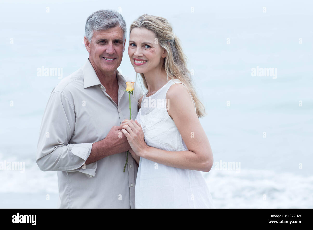 Happy couple smiling at camera and holding a flower Stock Photo - Alamy