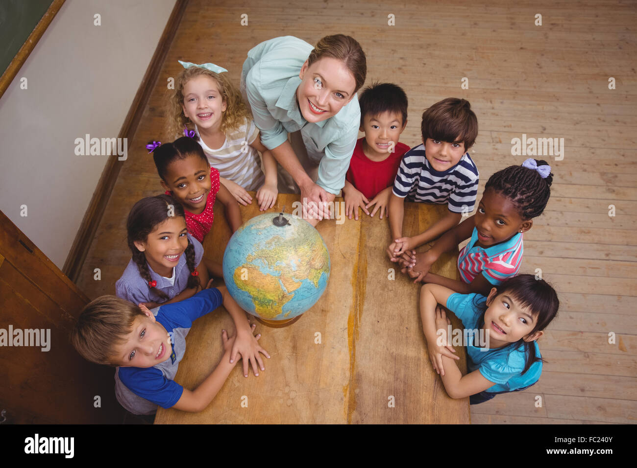 Cute pupils smiling around a globe in classroom with teacher Stock ...