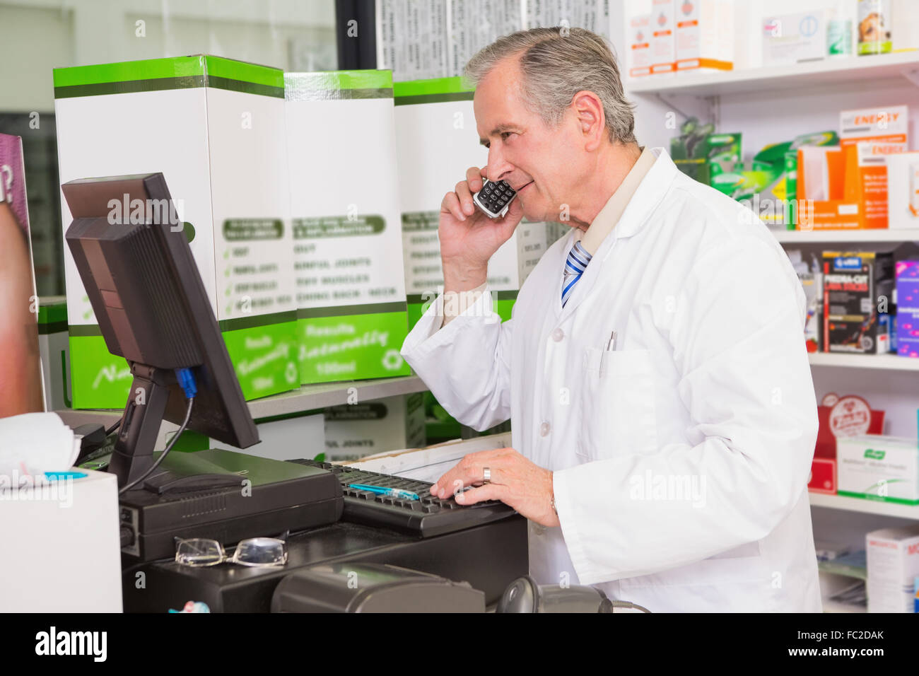 Senior pharmacist phoning while using computer Stock Photo