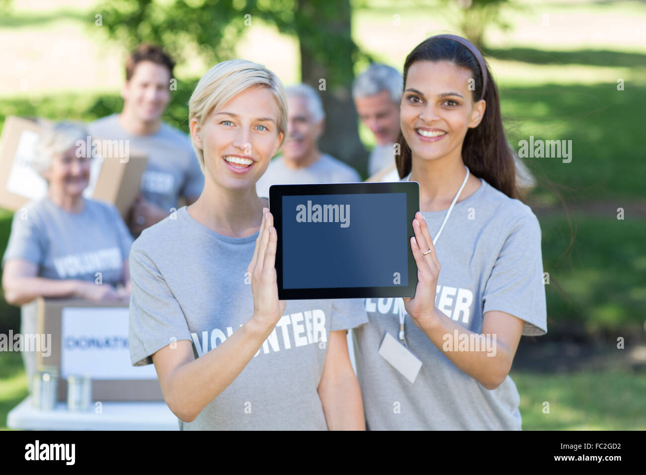 Happy volunteer friends showing tablet pc screen Stock Photo
