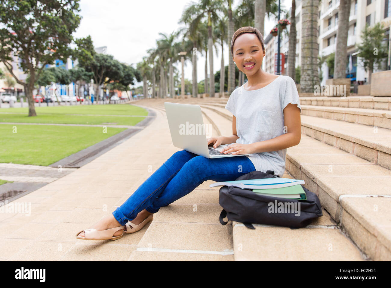 happy African college student with laptop sitting outdoors Stock Photo ...