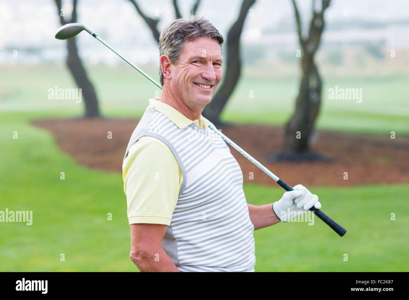Golfer standing and swinging his club smiling at camera Stock Photo