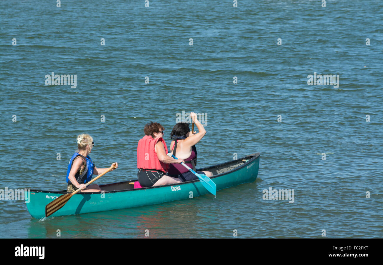 Three women  rowing  canoe on water Norfolk England Stock Photo