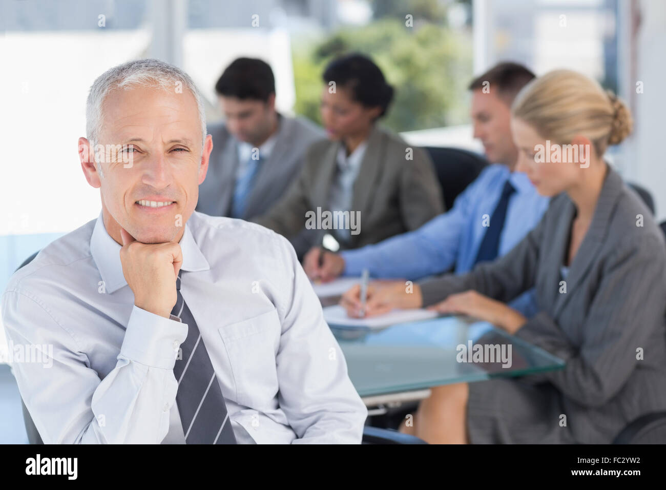 Businessman smiling at camera with colleagues behind Stock Photo - Alamy