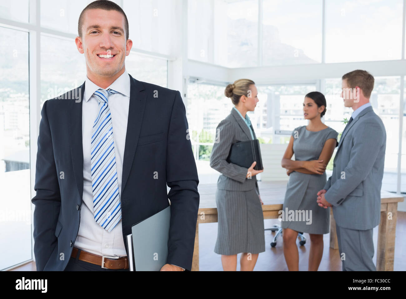 Businessman smiling at camera with colleagues behind him Stock Photo ...