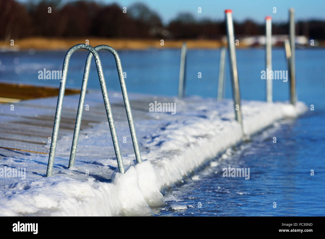 A swimming dock or bathing pier has frozen solid in the sea ice at winter. Seen from the sea with the main land in background. H Stock Photo