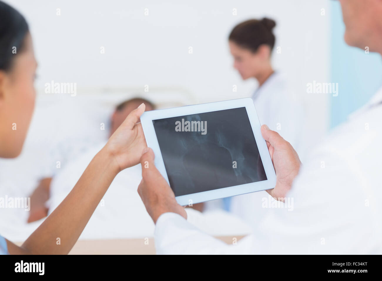 Doctor using digital tablet with colleagues and patient behind Stock ...