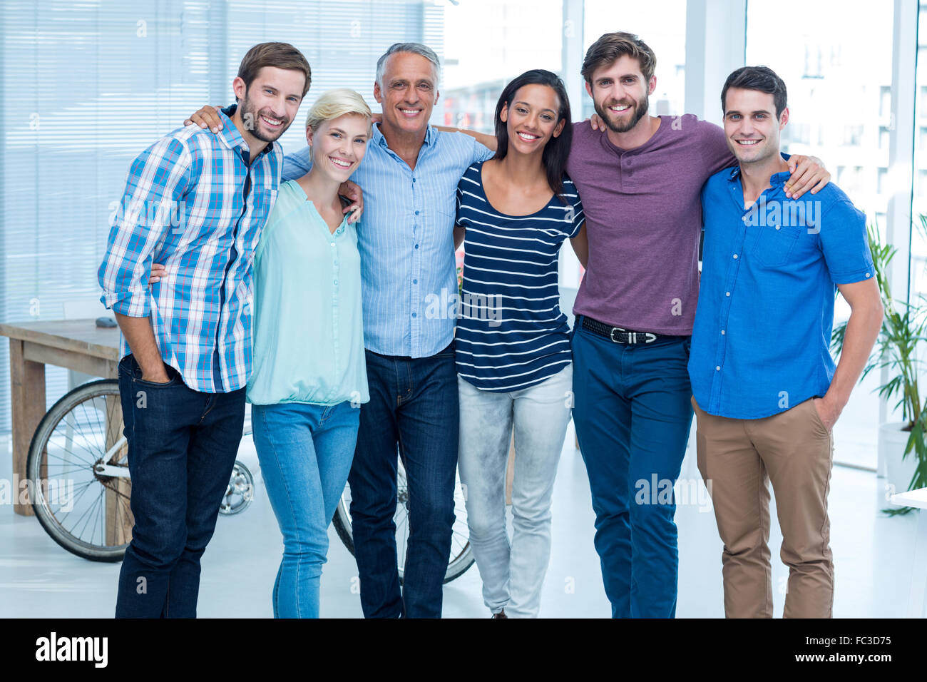 Happy business team with arms around in office Stock Photo - Alamy
