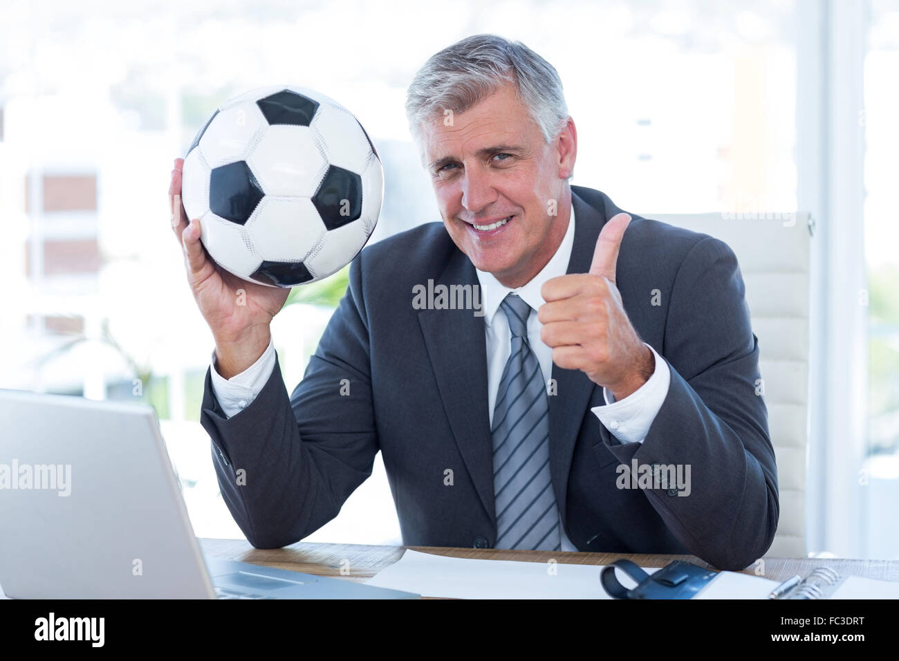Smiling businessman holding soccer ball with thumbs up Stock Photo - Alamy