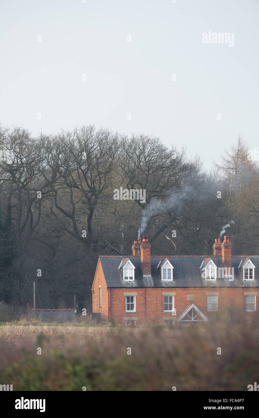 Smoke drifting from brick built country estate cottagers in late winters evening. Stock Photo