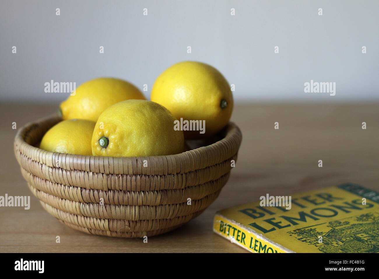 Lemons in a basket or bowl and book "Bitter Lemons" by Lawrence Durrell on a table Stock Photo