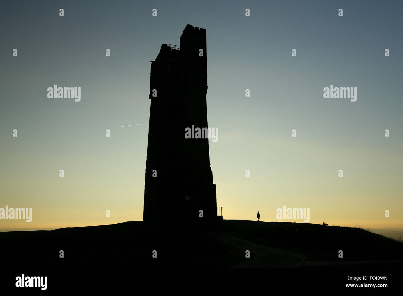 Huddersfield, West Yorks, UK. 20th January, 2016. A woman walks her dog as the sun sets over the Victoria Tower atop Castle Hill in Huddersfield in West Yorkshire, UK. The UK saw temperatures plummet to below -12 degrees for the second day in a row despite the bright sunny weather across much of the country. Credit:  Ian Hinchliffe/Alamy Live News Stock Photo