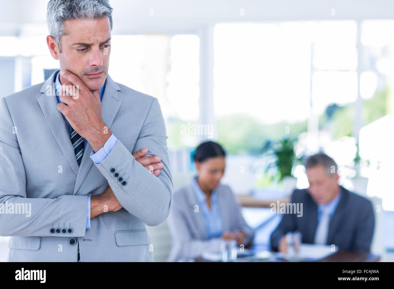 Thoughtful businessman with his colleagues behind him Stock Photo - Alamy