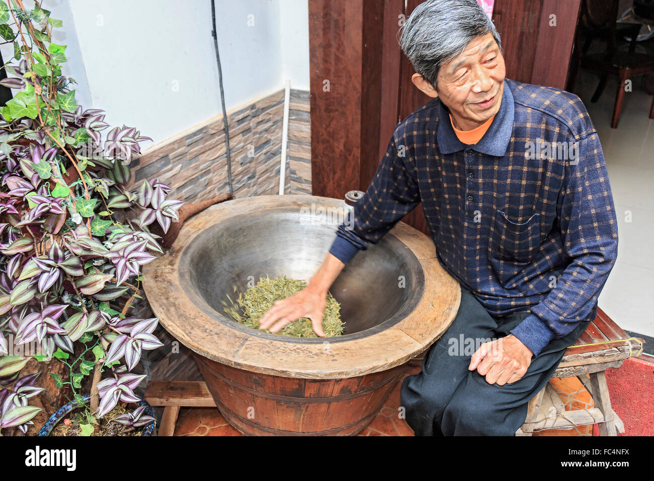 Electric wok style bowl used to cook fresh green tea leaves while someone stirs them by hand. Stock Photo