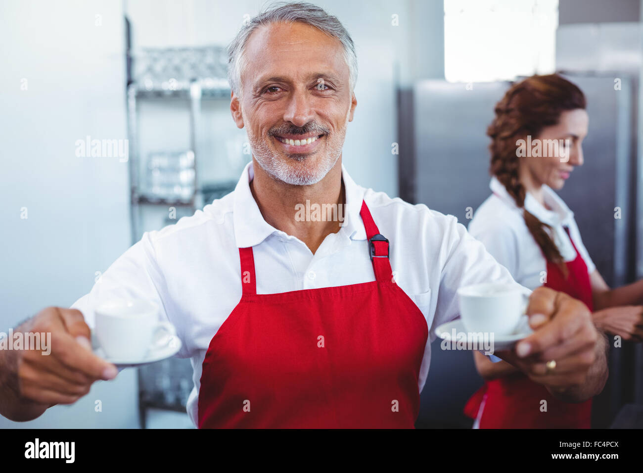 Smiling barista holding cups of coffee with colleague behind Stock Photo