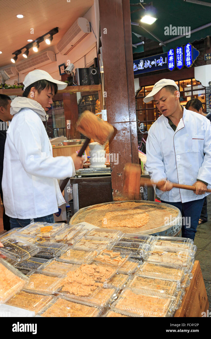 Men pound sesame seeds into flat paste which is then made into candy in shop along Qinghefang Ancient Street in Hangzhou, China Stock Photo