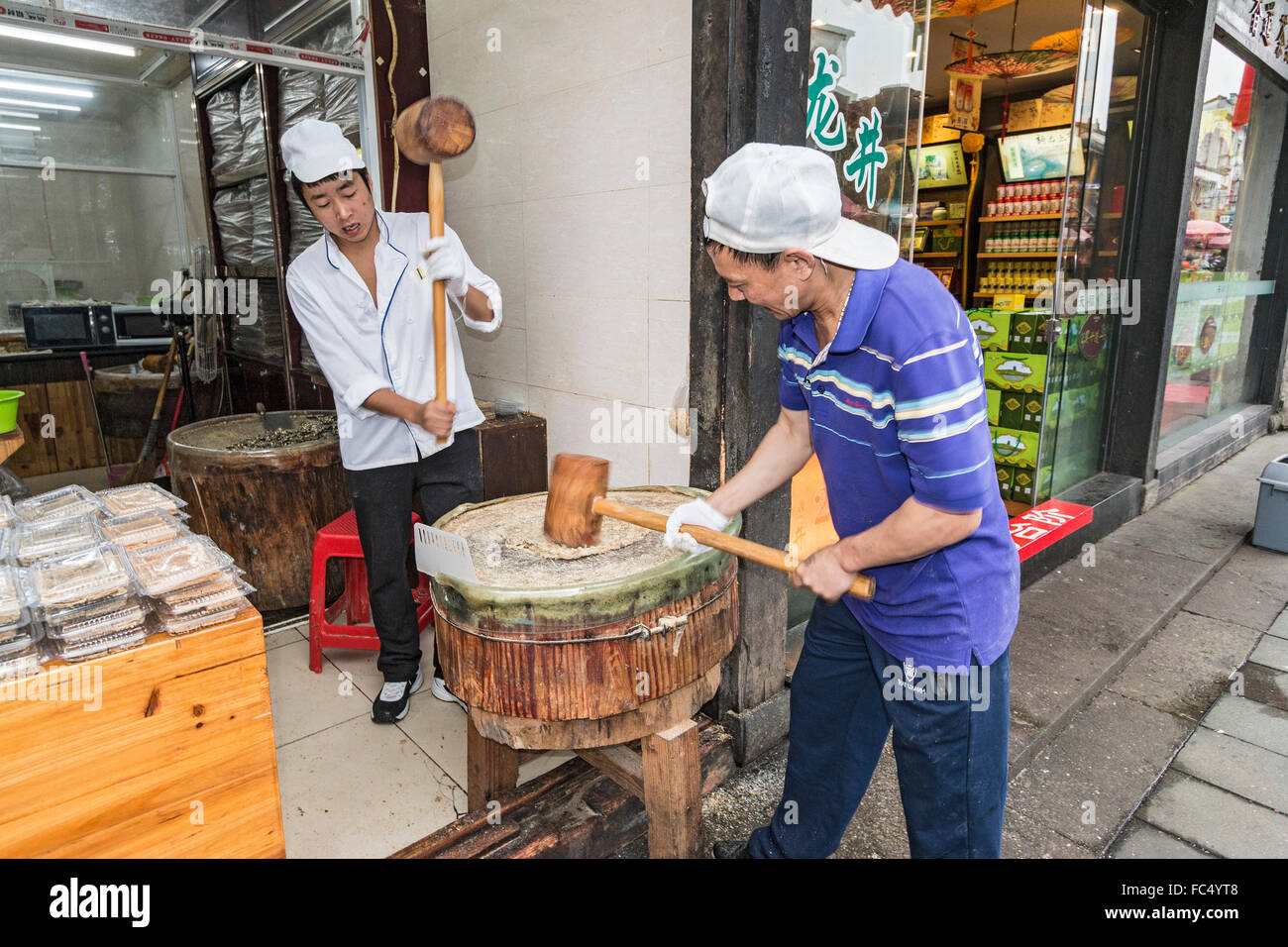 Men pound sesame seeds into flat paste which is then made into candy in shop along Qinghefang Ancient Street in Hangzhou, China Stock Photo