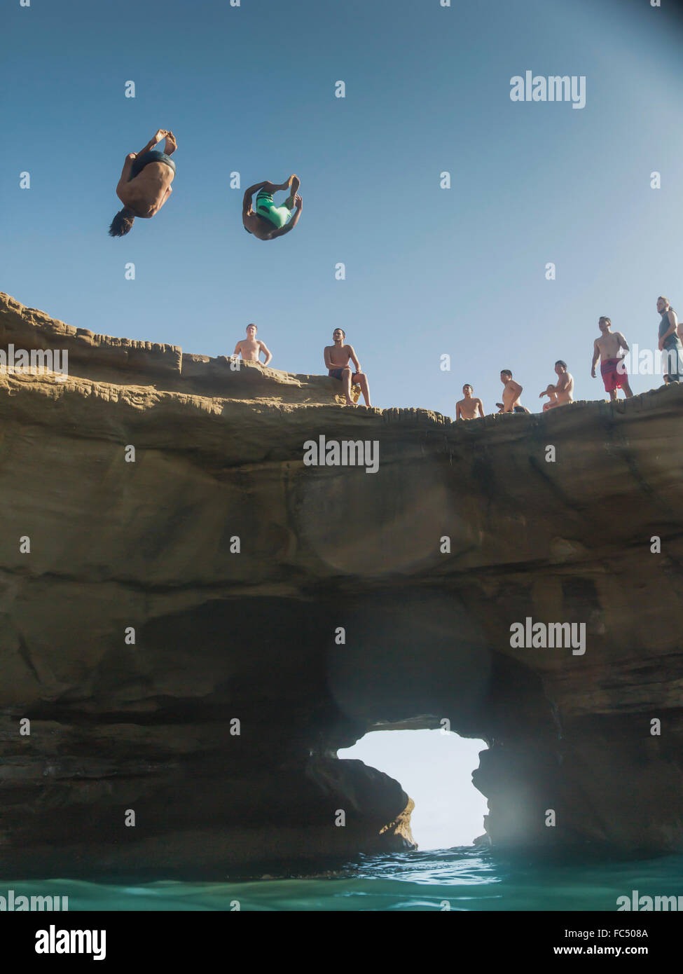 Two cliff divers do back somersault and dive from cliff at San Diego
