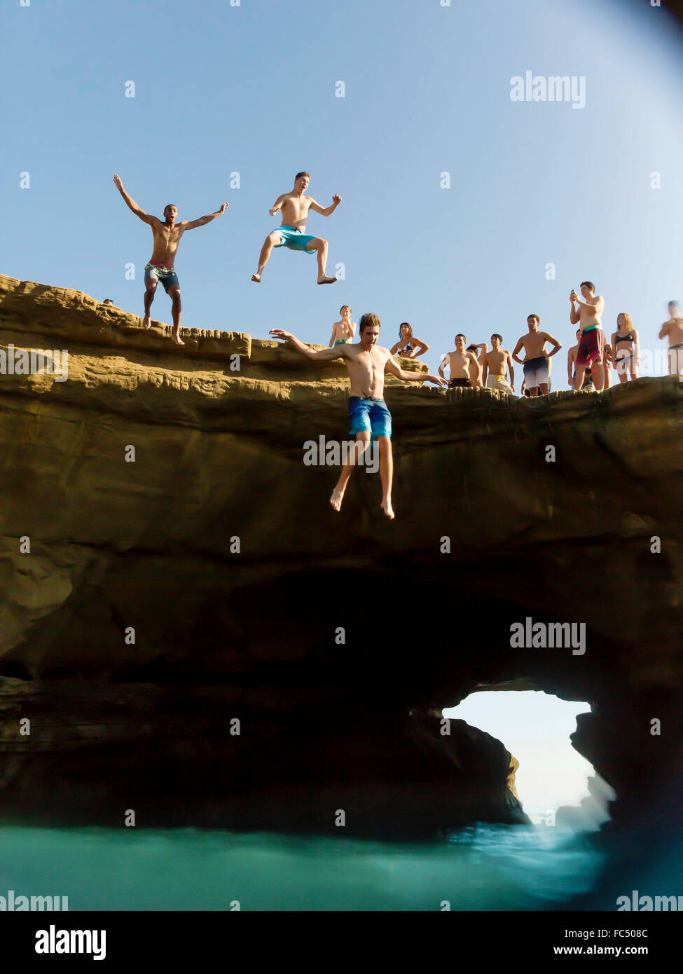 Three cliff divers dive from cliff at San Diego, California during