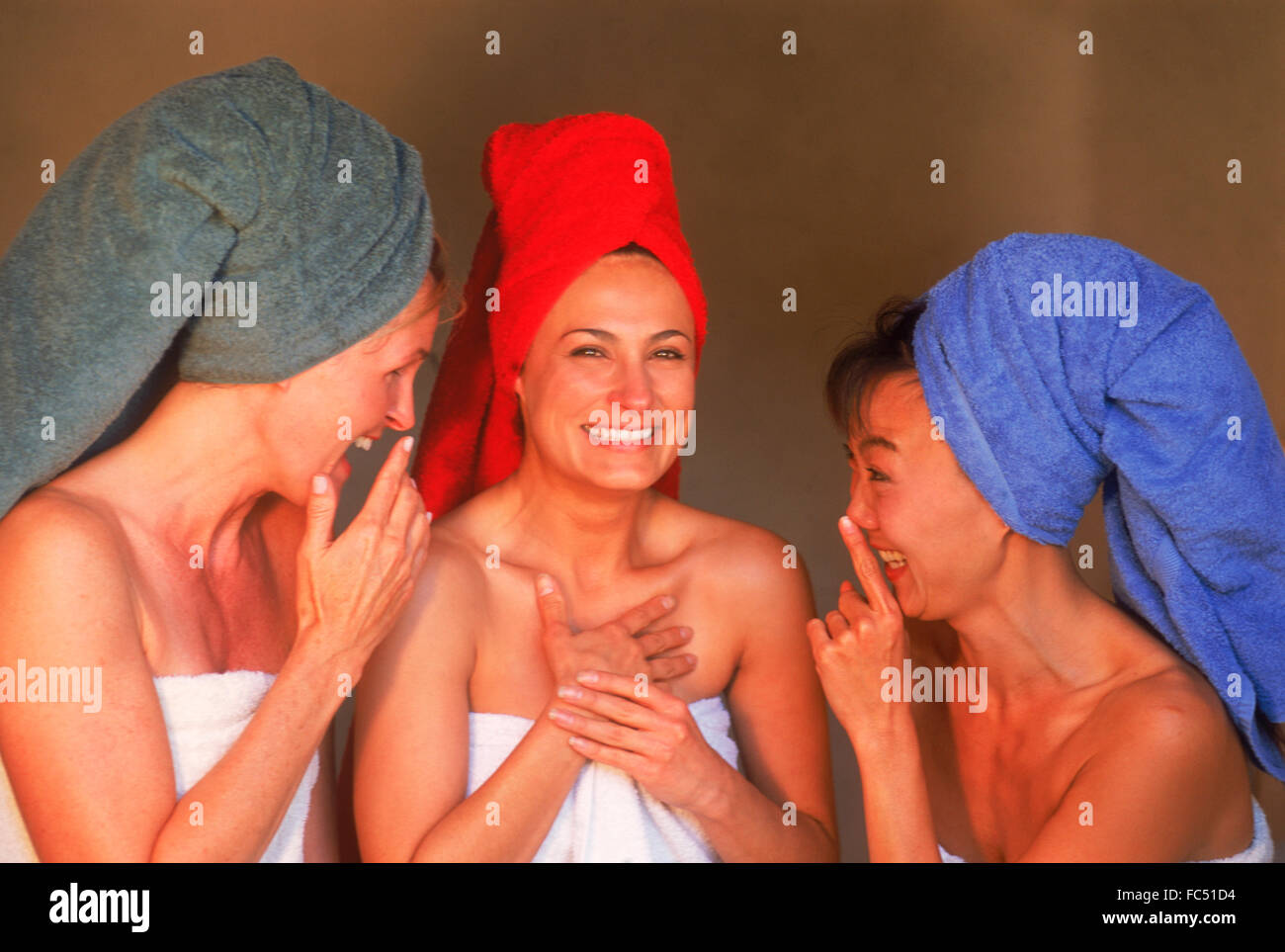 Three women of ethnic mix with colorful bath towels sharing gossip and laughing Stock Photo