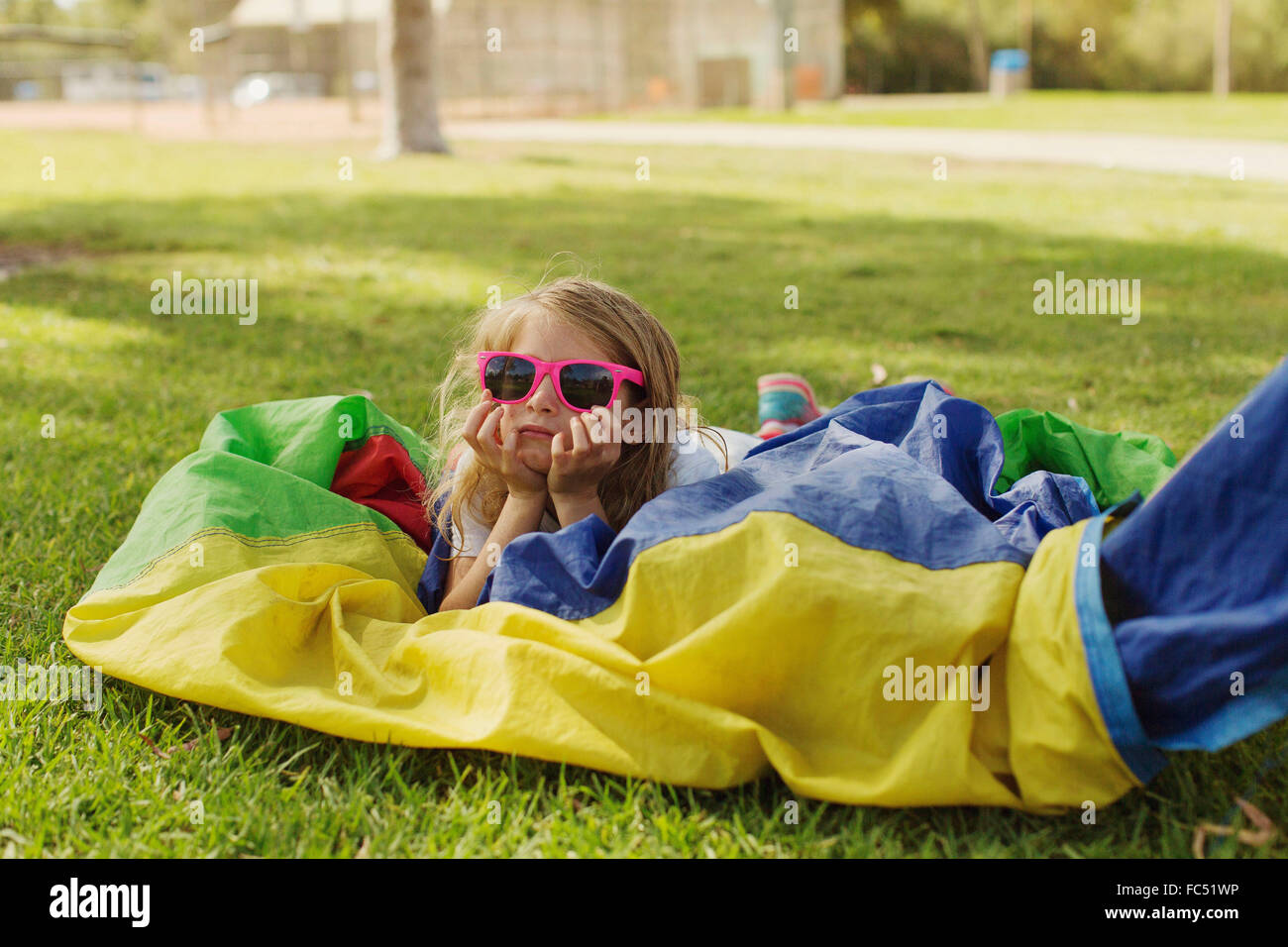 A little girl at summer camp in San Diego, California, lies in prone position on the ground over a tent with a pair of Stock Photo