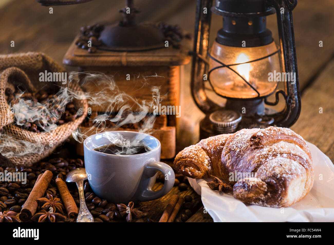 Rural Italian breakfast of coffee and croissant on a wooden table with a kerosene lamp. Stock Photo
